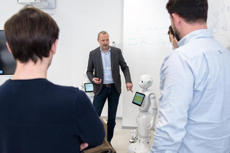 Prof. Dr. Patrick Jahn erklärt den Projektbeteiligten aus dem Kosovo den Einsatz des Roboters Pepper, an und mit dem an der Universitätsmedizin Halle im Bereich Gesundheitsforschung und Akzeptanz dieser Technologien geforscht wird.