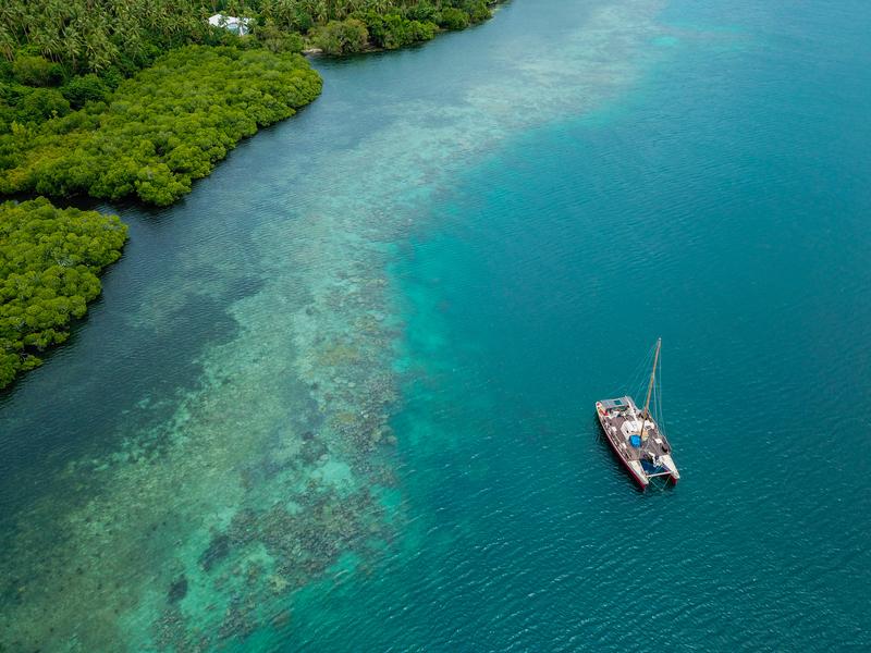 A catamaran (Vaka Motu) of the Okeanos Foundation off the reef fringe of Maskelyne Island 