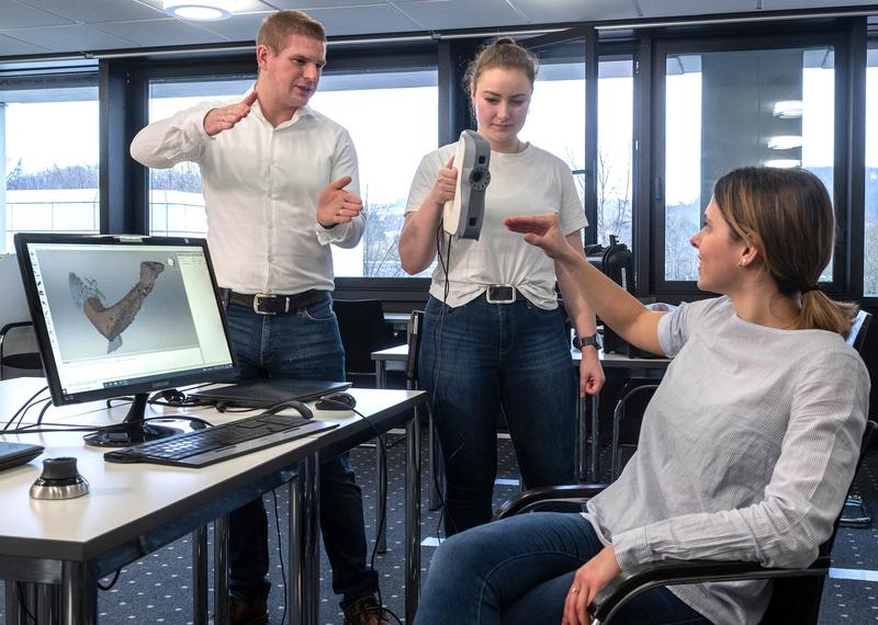 Markus Müller, Orthopädietechnik-Meister und Dozent an der PFH (li.) zeigt den Studentinnen Hannah Marienhagen (Mitte) und Leonie Litzenbauer die Methode zur digitalen Orthesenherstellung.