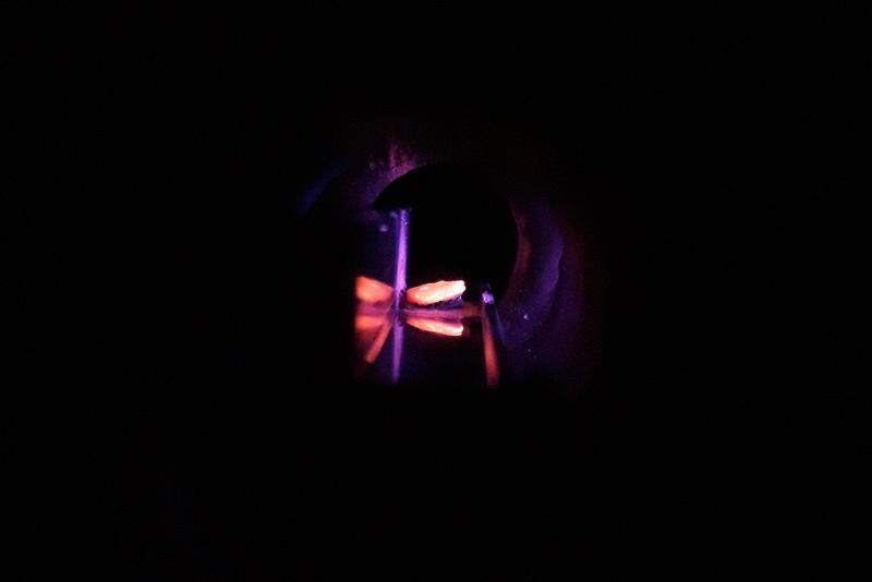 A uranium-molybdenum test target during fluorination with nitrogen trifluoride diluted with argon. At higher concentrations, the reaction is so violent that the target plate begins to glow, as can be seen in the picture.