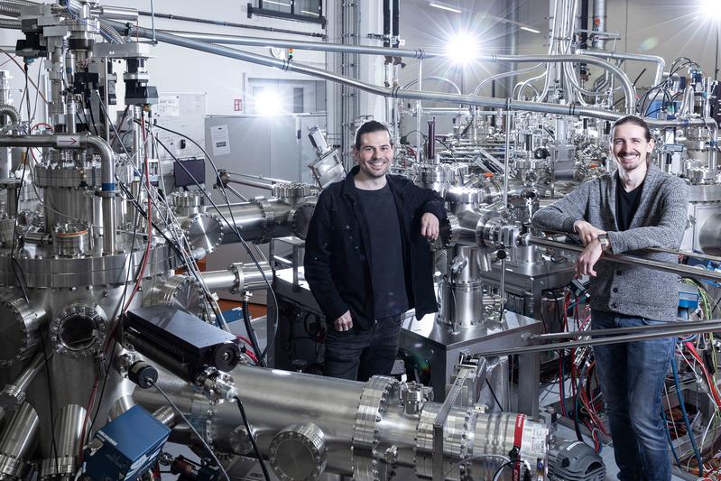 Dr. Peter Schüffelgen (l.) und Tobias Schmitt (r.) vor dem NanoCluster am Forschungszentrum Jülich, wo Kern-Komponenten des Hybrid-Qubits im Ultrahochvakuum gefertigt wurden.