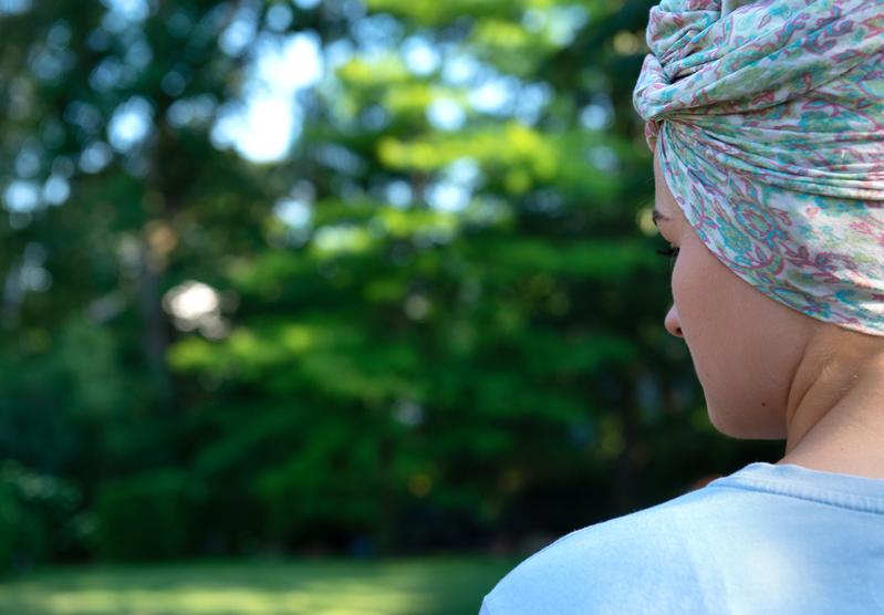 Das Bild zeigt eine junge Frau mit einem bunten Kopftuch, die auf eine Wiese schaut.
