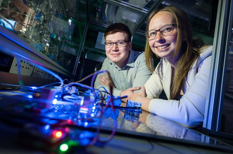 Dennis Arendes, Mitarbeiter am Lehrstuhl von Prof. Andreas Schütze (li.), und Dr. Caroline Schultealbert (3S GmbH) vor einer Gasmischanlage, mit deren Hilfe hochsensitive Gas-Sensoren kalibriert werden, wie sie auf der Hannover Messe vorgestellt werden.