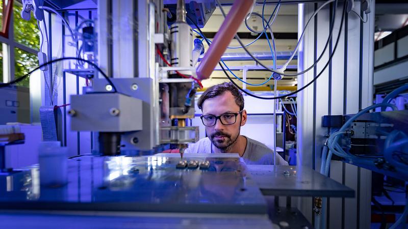 Johannes Rudolph, research associate at the Professorship of Electrical Energy Conversion Systems and Drives at Chemnitz University of Technology, observes the 3D printing of housings for power electronic components. 