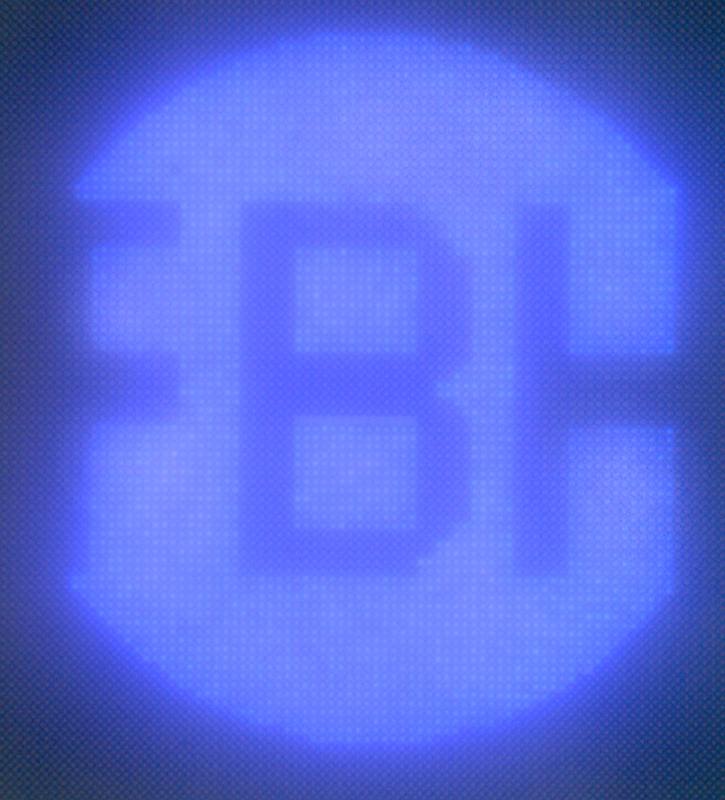 UV-leuchtendes Pixelarray von Mikro-LEDs mit einem Pixeldurchmesser von 1,5 µm und 2 µm Pitch in Form des FBH-Logos (Durchmesser 158 µm) unter dem Mikroskop.