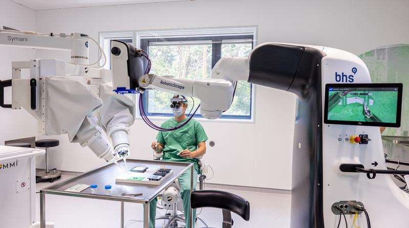 Dr. Maximilian Kückelhaus präsentiert bei einem „Trockentraining“ das neue Verfahren. Der Operationsroboter (rechts) ist mit einem robotischen Mikroskop (links) vernetzt.