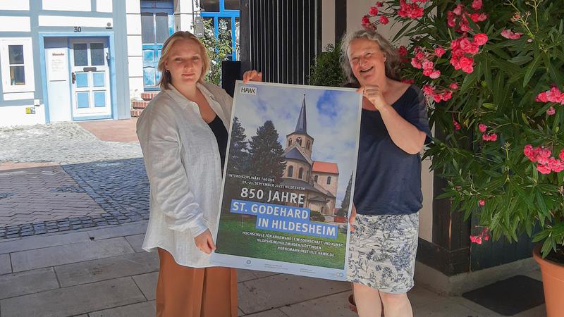 Dr. Angela Weyer (rechts), Leiterin des Hornemann Instituts, und Hannah Emmerich, wissenschaftliche Restauratorin, zeigen das Plakat zur Fachtagung.
