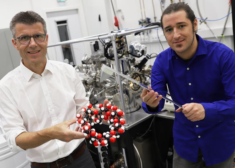 Prof. Dr. Dario Anselmetti von der Universität Bielefeld mit einem Kugelmodell eines Cyclodextrin-Moleküls – Basis der neuen Nanomembranen. Der Doktorand Niklas Biere hält das Modell des Kraftsensors, mit dem die Membran abgetastet wurde.