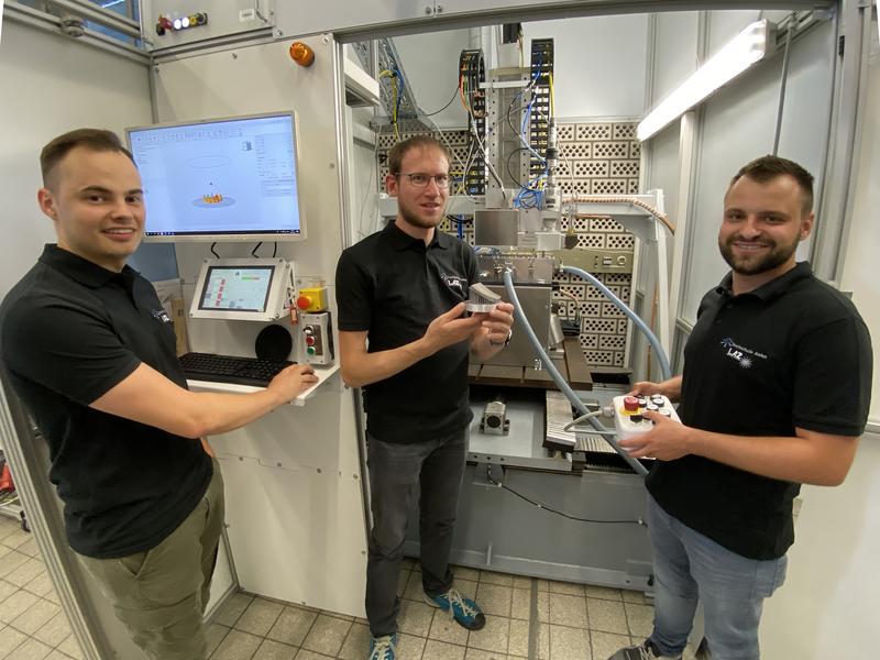 Robin Wenger, Markus Hofele und Patrick Grub (von links) aus dem Team des LaserApplikationsZentrums vor der Forschungsanlage mit einem Bauteil, das im 3D-Druckverfahren aus Metallpulver hergestellt wurde.