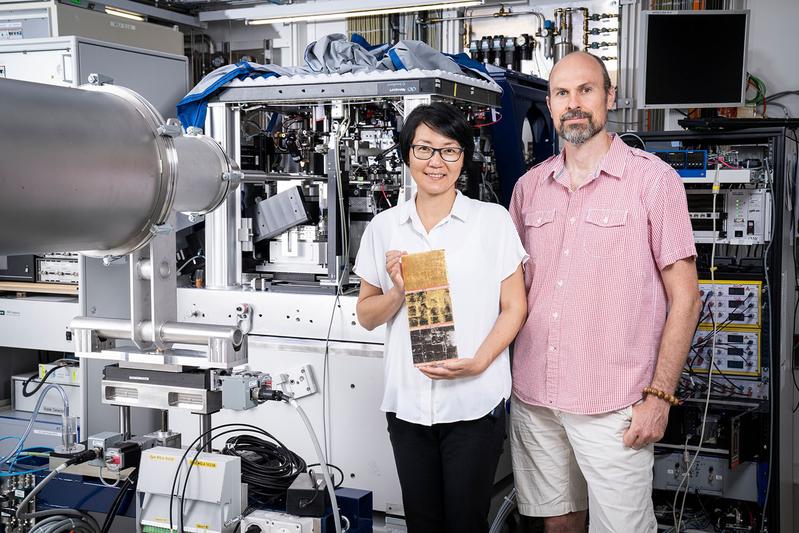 Qing Wu und Benjamin Watts an der cSAXS-Strahllinie, an der sie die Untersuchungen durchführten. Zur Demonstration hält Wu eine Platte mit jeweils einem Segment Blattgold, Zwischgold, Silber (von oben nach unten).