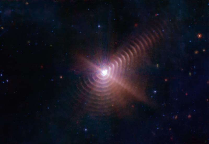 Die beiden Sterne in Wolf-Rayet 140 erzeugen alle acht Jahre bei ihrer größten Annäherung ringförmige Staubschalen, wie auf diesem JWST-Bild zu sehen. Dabei kollidieren die Sternwinde, wodurch das Gas komprimiert wird und zur Entstehung von Staub führt.