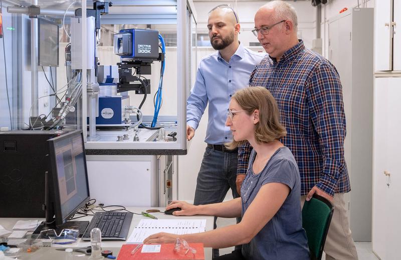 Das Foto zeigt Dr. Janio Venturini (links), Prof. Tom Nilges und Erstautorin Anna Vogel vor einem Messgerät zur Bestimmung von Kristallstrukturen, einem sogenannten Einkristalldiffraktometer. 