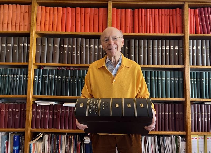 Gerd Plewig in seinem Büro mit der 1555 in Basel gedruckten zweiten Auflage des Werkes von Andreas Vesalius "De humani corporis fabrica libri septem".