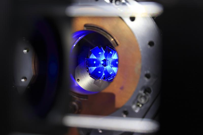 Blick auf eine Wolke von blau fluoreszierenden Strontiumatomen. Sie werden mithilfe von Laserstrahlen bis auf Temperaturen dicht am absoluten Nullpunkt gekühlt. Gut sichtbar ist der Kranz aus sechs Spiegeln, die die Strahlen reflektieren. 