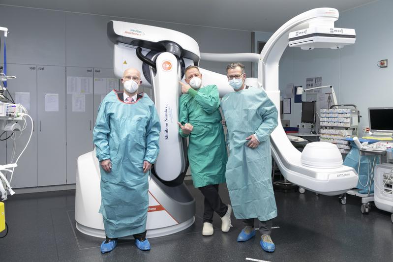 Carsten Bertram (Siemens Healthineers), Prof. Dr. Eric Verhoeven und Prof. Dr. Achim Jockwig (v. l.) im Hybrid-OP vor einem der zwei neuen Bildgebungs-roboter