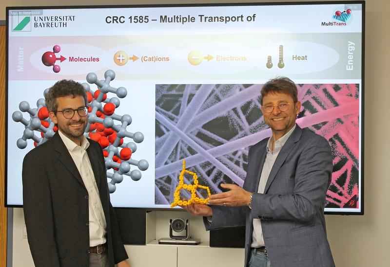 Prof. Dr. Markus Retsch (left) and Prof. Dr. Jürgen Senker (right), in the centre (yellow): a 3D-printed model of the porosity of covalent organic frameworks.