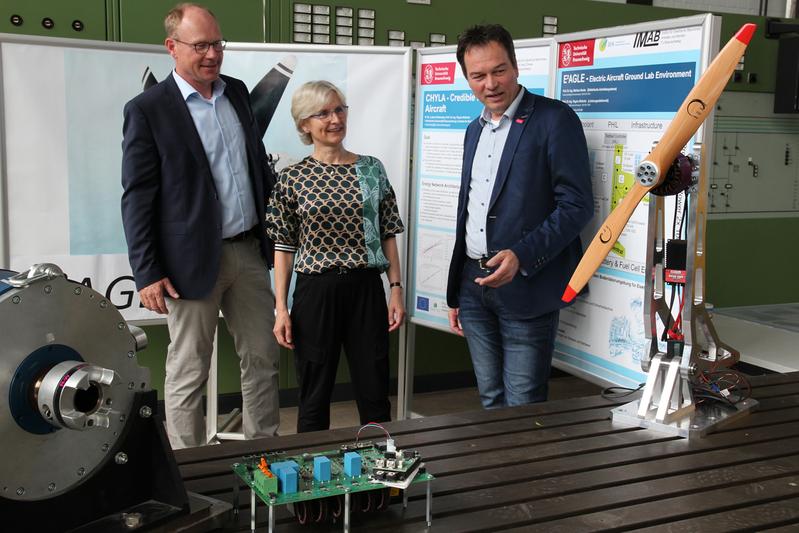 Im Laborraum des Instituts für Elektrische Maschinen, Antriebe und Bahnen wird ein Teilsystem von E2AGLE errichtet. Prof. Markus Henke, Prof. Regine Mallwitz sowie SE2A Clustersprecher Prof. Jens Friedrichs mit den ersten Komponenten des Großgeräts E2AGLE