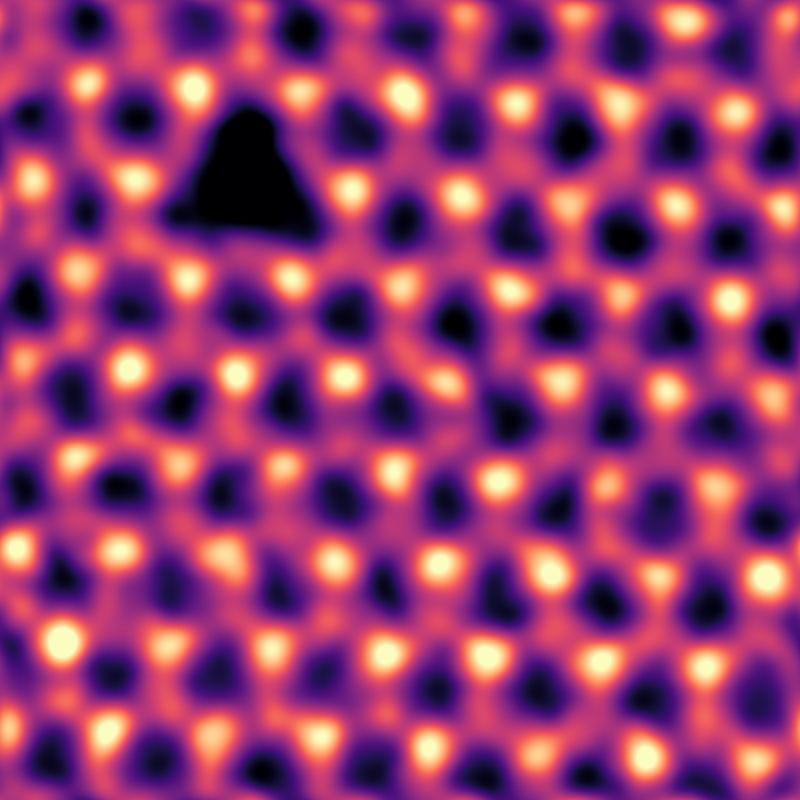 Einzelne Stickstoff-Leerstellen (dreieckiger dunkler Kontrast oben links), die durch Elektronenbestrahlung in hexagonalem Bornitrid erzeugt wurden. Gefiltertes und gefärbtes rastertransmissionselektronenmikroskopischen Bild.