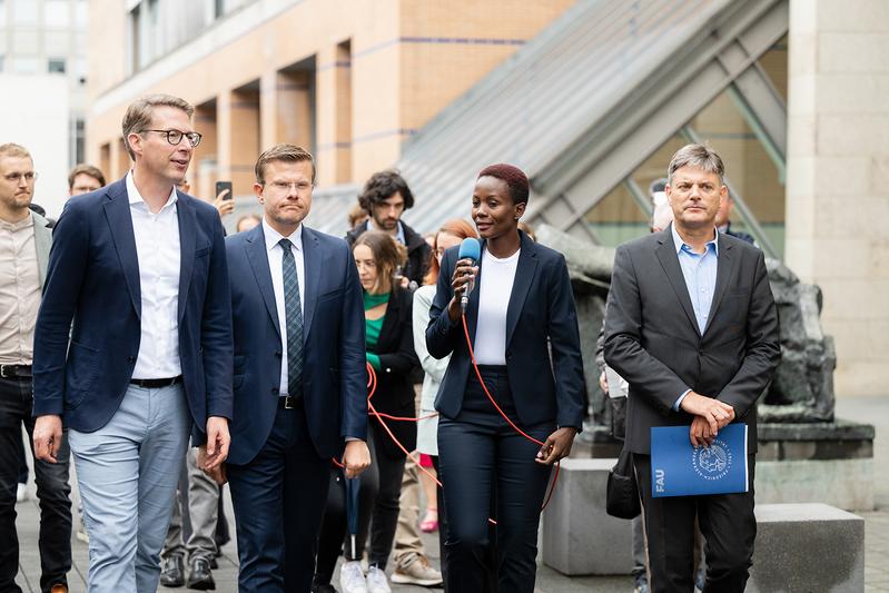 FAU-Doktorandin Aneth Lwakatare-Thumm erklärt Wissenschaftsminister Markus Blume, Nürnbergs Oberbürgermeister Marcus König und FAU-Präsident Joachim Hornegger (v.l.) Säule Art. 25 „Recht auf angemessenen Lebensstandard“ der Menschenrechte.