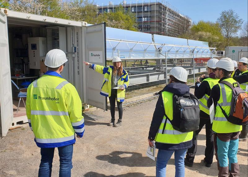 Mit Besuchern besichtigt Arianna Passamonti die Gesamtanlage samt Solarthermieanlage, die ihre im Sommer gesammelte Wärme in 64 Meter Tiefe in Grubenwasser speichert. Bild: K. Schinarakis/Fraunhofer IEG