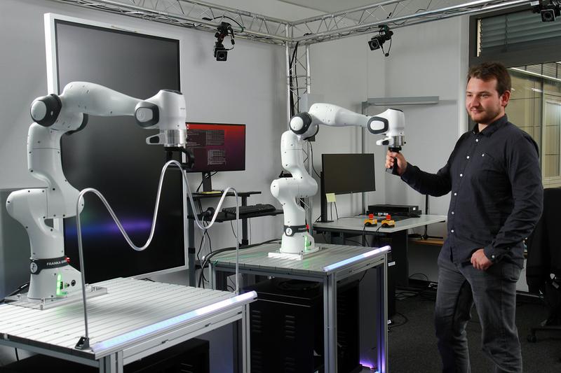 Jan Petershans, wissenschaftlicher Mitarbeiter im Team, zeigt den Demonstrator, der aus zwei kollaborativen Roboterarmen besteht. Ein Roboterarm lässt sich durch die Führung des anderen von Menschenhand steuern.