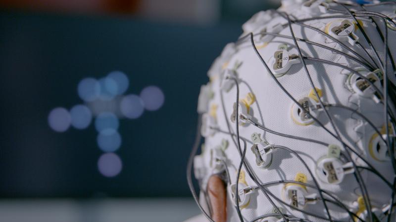 Ein Experiment zu passiven Gehirn-Computer-Schnittstellen/Passive BCIs. Auf der Kopfhaut aufliegende Elektroden zeichnen die Gehirnaktivität auf und übersetzen diese in Echtzeit in Veränderungen, die auf dem Computerbildschirm sichtbar sind.