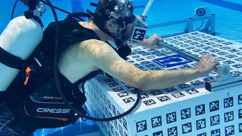 Prof Andreas Nüchter presenting the new VR application in the JMU university swimming pool. A lowered block with tracking codes can be seen in front of him - Nüchter perceives it as part of a space station via his VR headset.