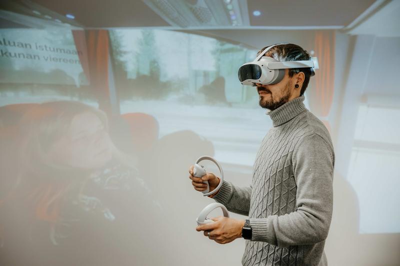 Der Projektmitarbeiter Hannes Tegelbeckers probiert mit einer VR-Brille den entwickelten Prototypen aus. Auf der Leinwand im Hintergrund ist zu erkennen, was er sieht.