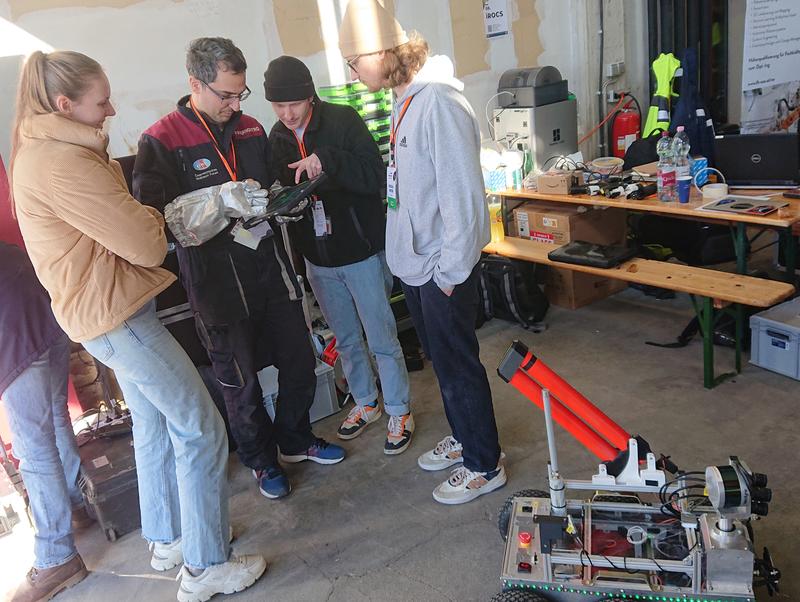 Die Studierenden (v.l.n.r.) Carolin Bösch, Julius Arzberger und Pascal Meyer leiten Analog-Astronaut Simone Paternostro (Zweiter v.r.) beim Test des Handbedienungsgeräts mit Touchscreen mit seinem Handschuh an.