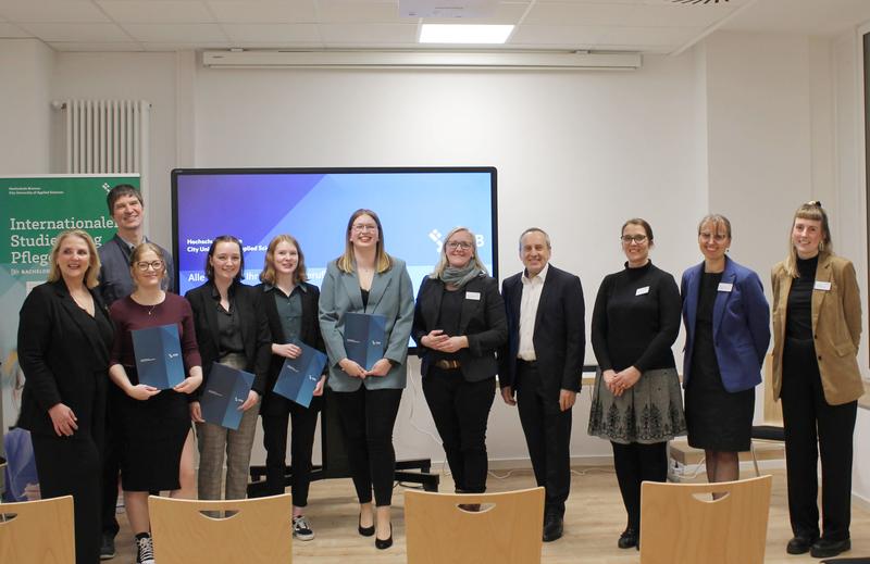 Fototermin mit Absolventinnen (blaue Mappen) des Internationalen Bachelorstudiengangs Pflege (ISPF) und Mitarbeitenden der Hochschule Bremen (HSB). Darunter der Rektor Konrad Wolf und die Studiengangsleiterin Claudia Stolle-Wahl (4. und 3. von rechts).