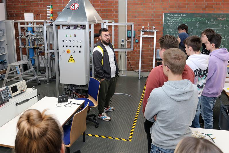 Maschinenbau-Student Awat Cheikhi (Mitte) beantwortet während der Besichtigung des Wasserstoff-Labors der THWS die Fragen der Schülerinnen und Schüler 