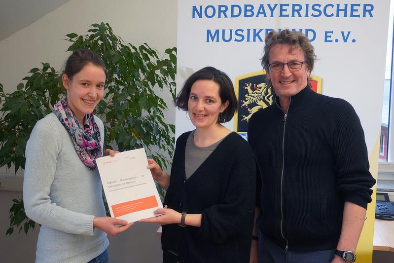 Dr. Laura Blauth von der THWS übergab Monika Feldmeier und Gerhard Cäsar vom Kooperationspartner Nordbayerischer Musikbund (NBMB) die fertige Handreichung