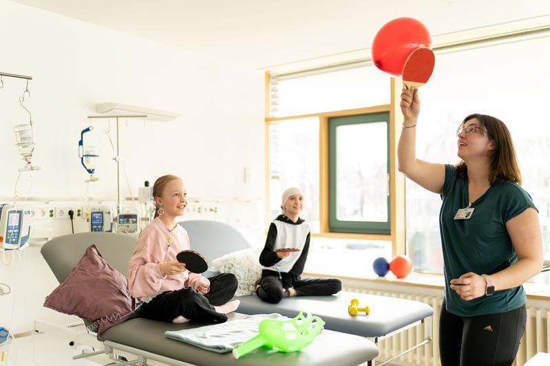 Sporttherapeutin Sabine Barde (r.) lenkt Lotta und Emily während ihrer Chemotherapie in der Tagesklinik der Kinderonkologie am Uniklinikum Dresden mit einem Ballspiel ab.