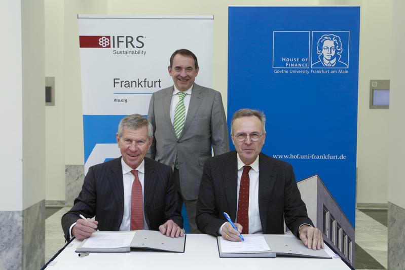 Erhard Schipporeit (links) vom IFRS und Prof. Rainer Klump, Geschäftsführender Direktor des House of Finance, beim Unterzeichnen des MoU. Finanzminister Prof. R. Alexander Lorz (im Hintergrund) freut sich über das entstehende Netzwerk.