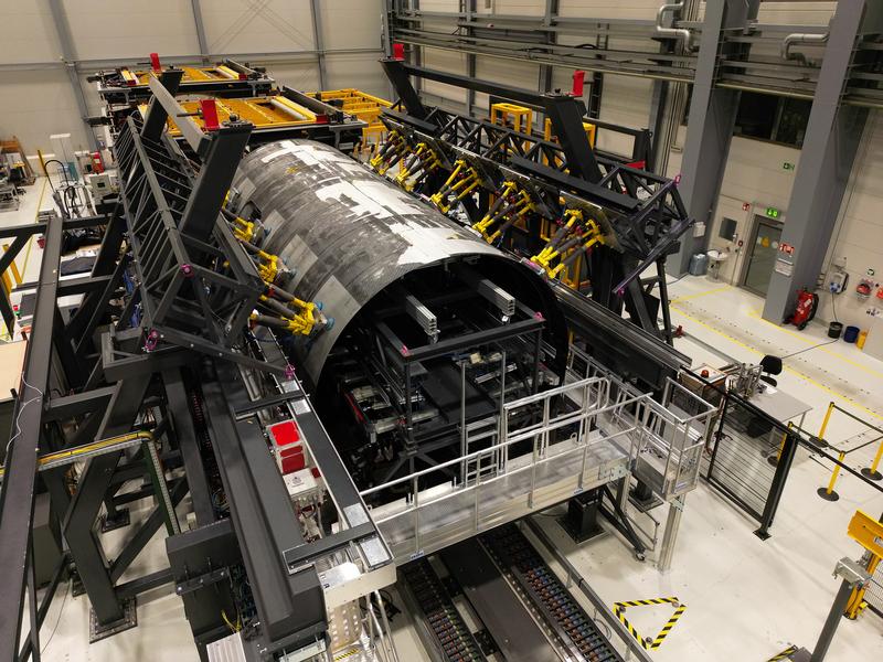 The MultiFAL assembly research platform with inserted thermoplastic fuselage shells of the MFFD at Fraunhofer in Stade. The yellow hexapod robots for holding and high-precision adjustment of the shape and position of the upper shell are clearly visible