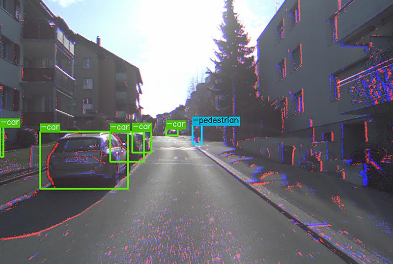 The image shows both color information from the color camera and events (blue and red dots) from the event camera; bounding boxes show the detection of cars by the algorithm. 