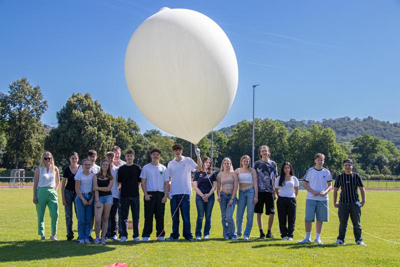 Eine Gruppe Schülerinnen und Schüler mit MINTplus-Begleiterin Maria Müller (ganz links) und dem selbst gebauten Wetterballon