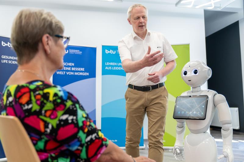 Interaktion Mensch - Roboter. Simulationspatientin (li.) im Dialog mit Pepper zum Trinkverhalten. Der BTU-Pflegewissenschaftler Jörg Matthäi gibt Erläuterungen. 