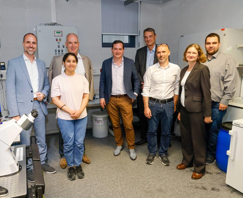 Wissenschaftsminister Clemens Hoch (l.), JGU-Präsident Prof. Dr. Georg Krausch (3.v.l.) und JGU-Vizepräsident Prof. Dr. Stefan Müller-Stach (5.v.l.) mit Wissenschaftler*innen des Exzellenzprojekts CoM2Life