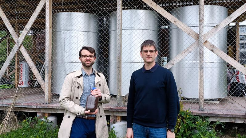 Die ETH-Forschenden Samuel Heiniger (links, mit einem Glas Eisenerz) und Professor Wendelin Stark vor den drei Eisenreaktoren am Campus Hönggerberg der ETH Zürich. 