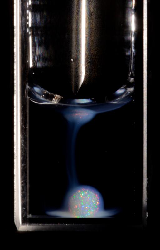 An opalescent drop, several millimeters in diameter, under white light illumination. While there are a few individual reflections visible at the drop rim, the drop interior cannot be observed.