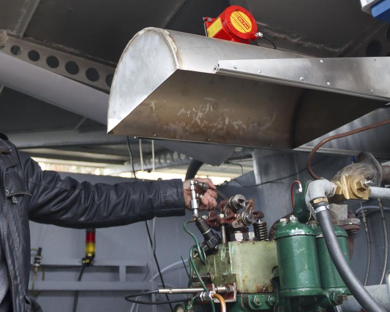 Versuchsaufbau am klassischen Dieselmotor, über dem sich die Wasserstoffauffangwanne mit Sensor befindet. In der Hand ist das HD-Eindüs-Ventil zu erkennen.