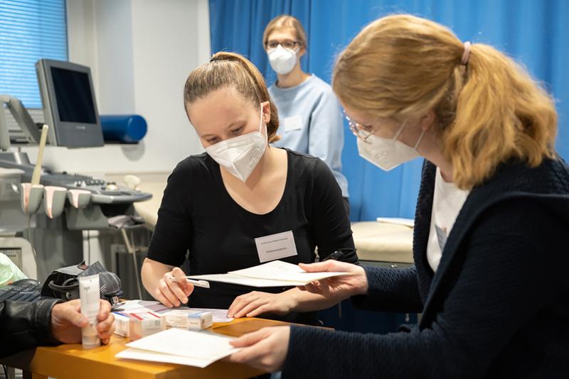 MHH-Studentin, die mit einer Tutorin aus fortgeschrittenen Studienjahren und einer Ärztin in der StuPoliH vor einem Patienten (nicht auf dem Bild) sitzt. 