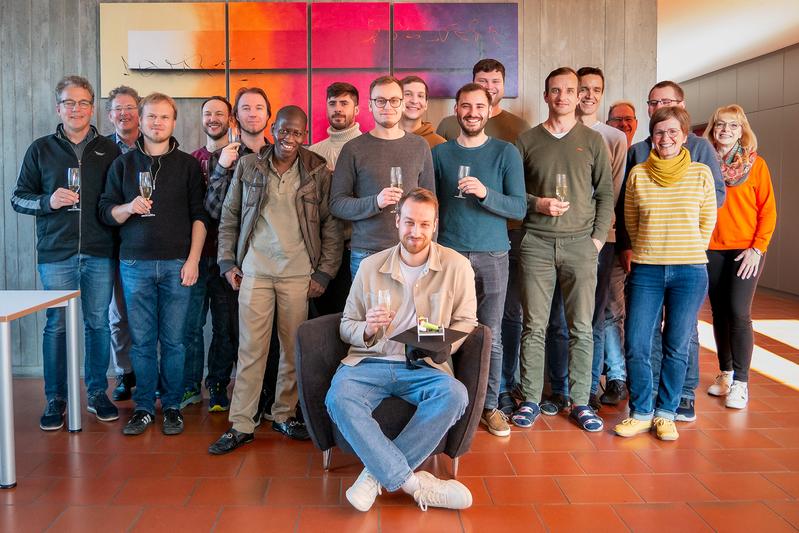 Die Mitarbeitenden des TTZ-EMO beglückwünschen Dr. Thiemo Hein (vorne) zu seiner hervorragenden Leistung mit alkoholfreiem Sekt und symbolischem Doktorhut mit einer Batterie 