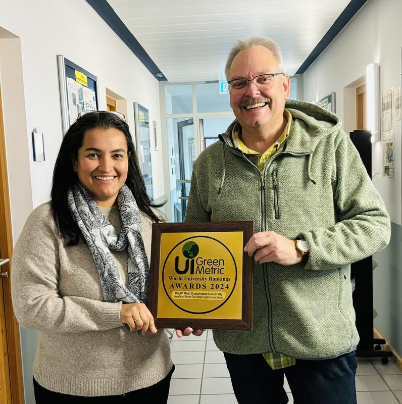 Nachhaltigkeitsbeauftragter Prof. Dr. Klaus Helling nimmt am UCB stolz die Plakette von Jackeline Martinez entgegen.