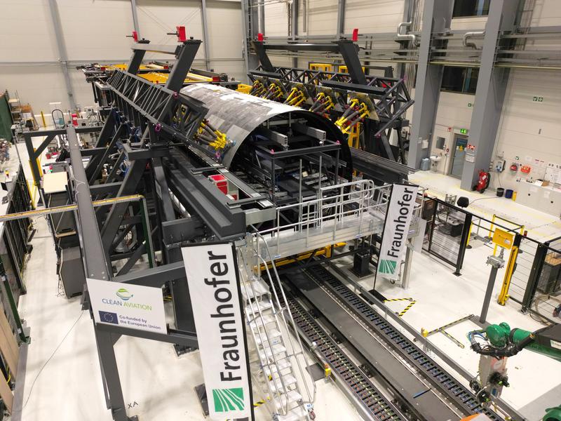 Montage-Forschungsplattform mit eingerüsteten thermoplastischen Rumpfschalen des »MFFD« bei der Fraunhofer-Gesellschaft in Stade. Gut erkennbar sind die gelben Hexapod-Roboter zum Halten und hochpräzisen Einstellen von Form sowie Lage der Oberschale 