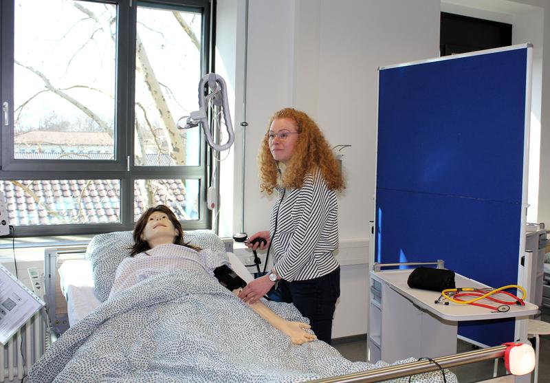 Praxiskoordinatorin Jacqueline Reißer gibt Einblick in eine praktische Übung im Skills- und Simulationszentrum: Hier trainieren die Studierenden im 1. Semester Pflege beispielweise das richtige Blutdruckmessen. 