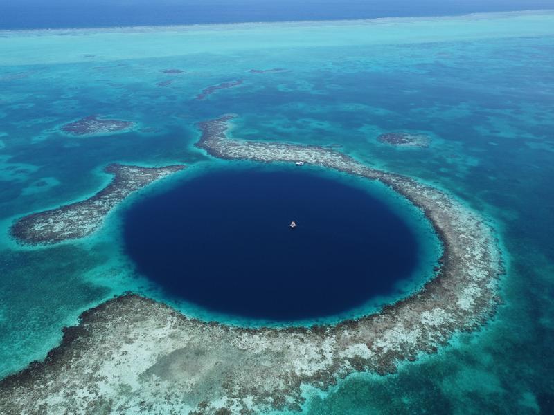 Drohnenaufnahme aus 200 Metern Höhe auf das „Great Blue Hole“ mit der in der Mitte verankerten Bohrplattform. Im Hintergrund ist der Rand des Lighthouse Reef-Atolls zu sehen