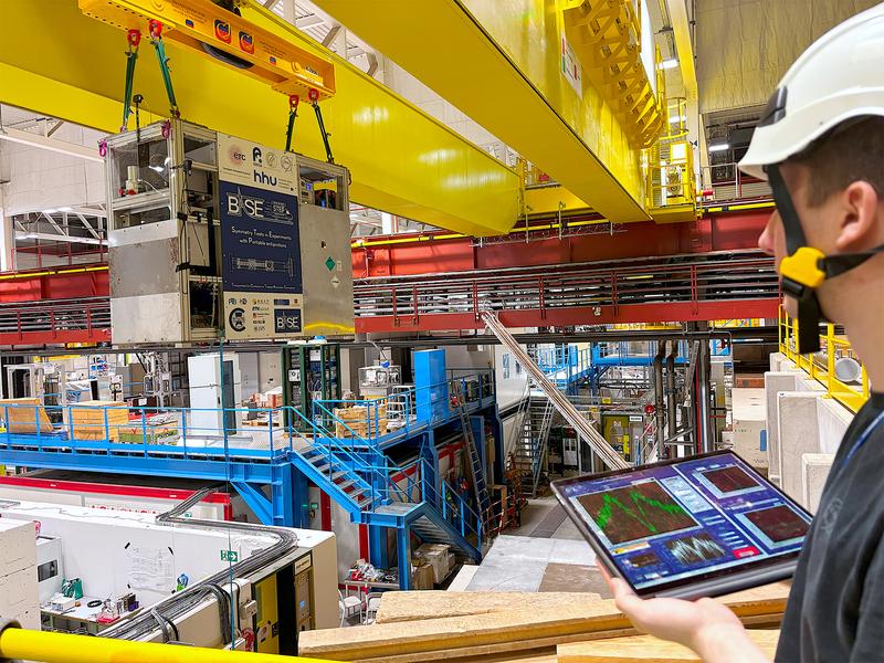 Am Kran: Das autonome Penning-Fallensystem BASE-STEP wird am CERN zum Lkw transportiert. Über ein Tablet kann HHU-Physiker Marcel Leonhardt (rechts) den Status des Geräts und den Einschluss der Protonen kontrollieren.