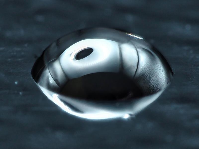 Ein Tropfen, wie er im Raman-Mikroskop untersucht wurde, während der Verdunstung. Als Substrat wurde beschichtetes Glas genutzt. Die dunkle Stelle markiert die ungefähre Eintrittsstelle des Lasers.